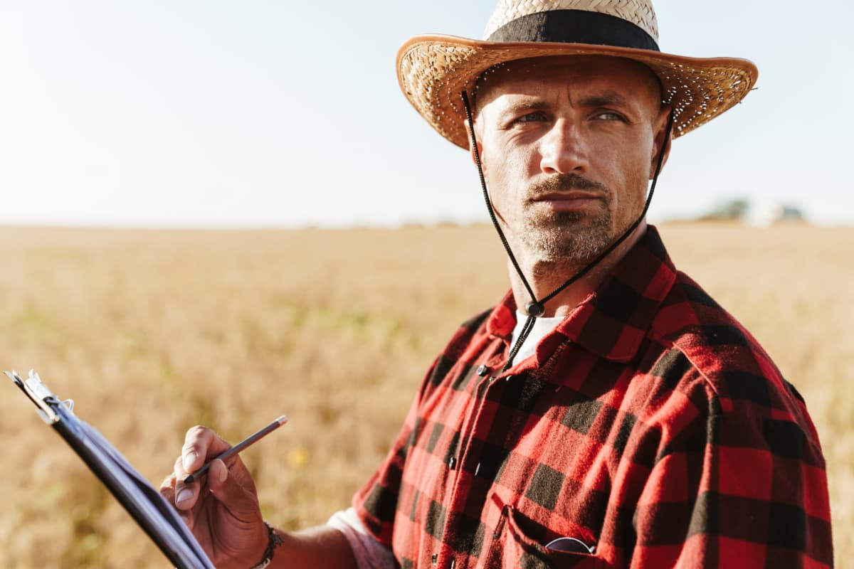 A farmer in a field making calculations.